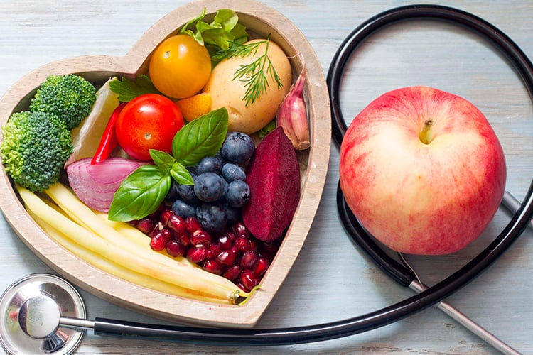 Verduras, frutas y hortalizas dentro de un corazón hecho de madera junto a un estetoscopio que rodea a una manzana