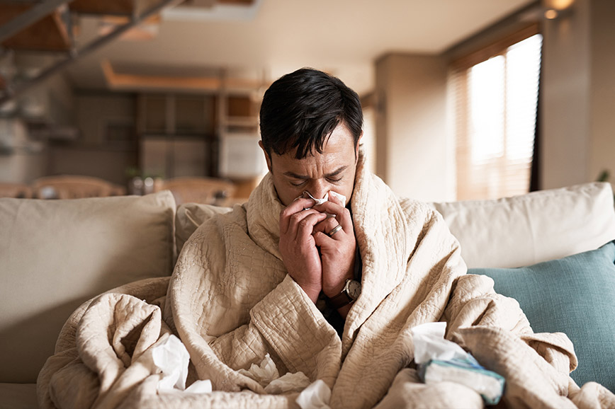 A man with the ‘flu wrapped in a blanket and blowing his nose.