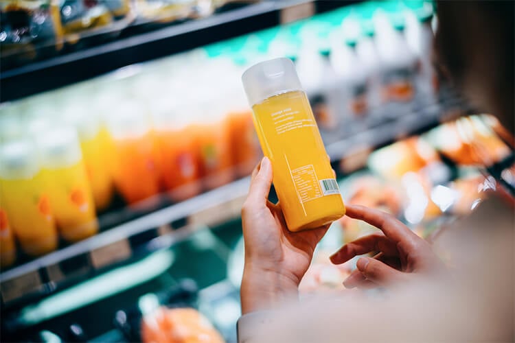 Mujer en el supermercado lee el etiquetado nutricional trasero de un jugo de frutas