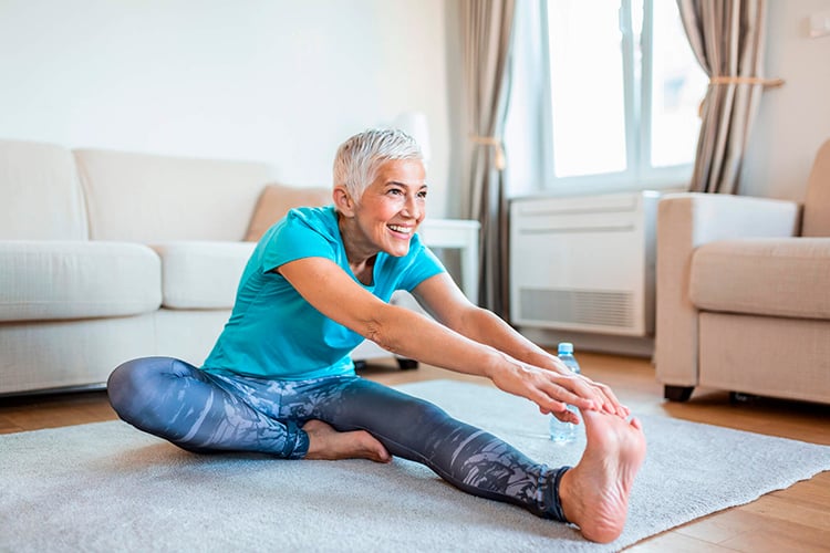 Mujer mayor sentada en el suelo, estira sus músculos antes de hacer deporte
