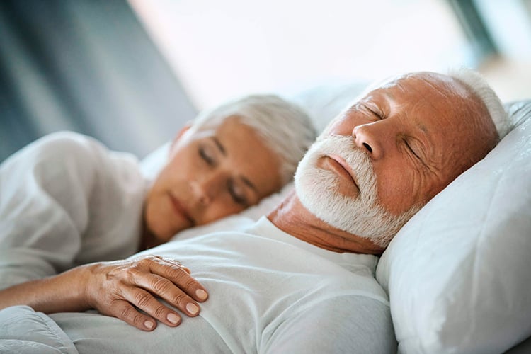 Hombre mayor duerme plácidamente con su mujer recostada en su pecho