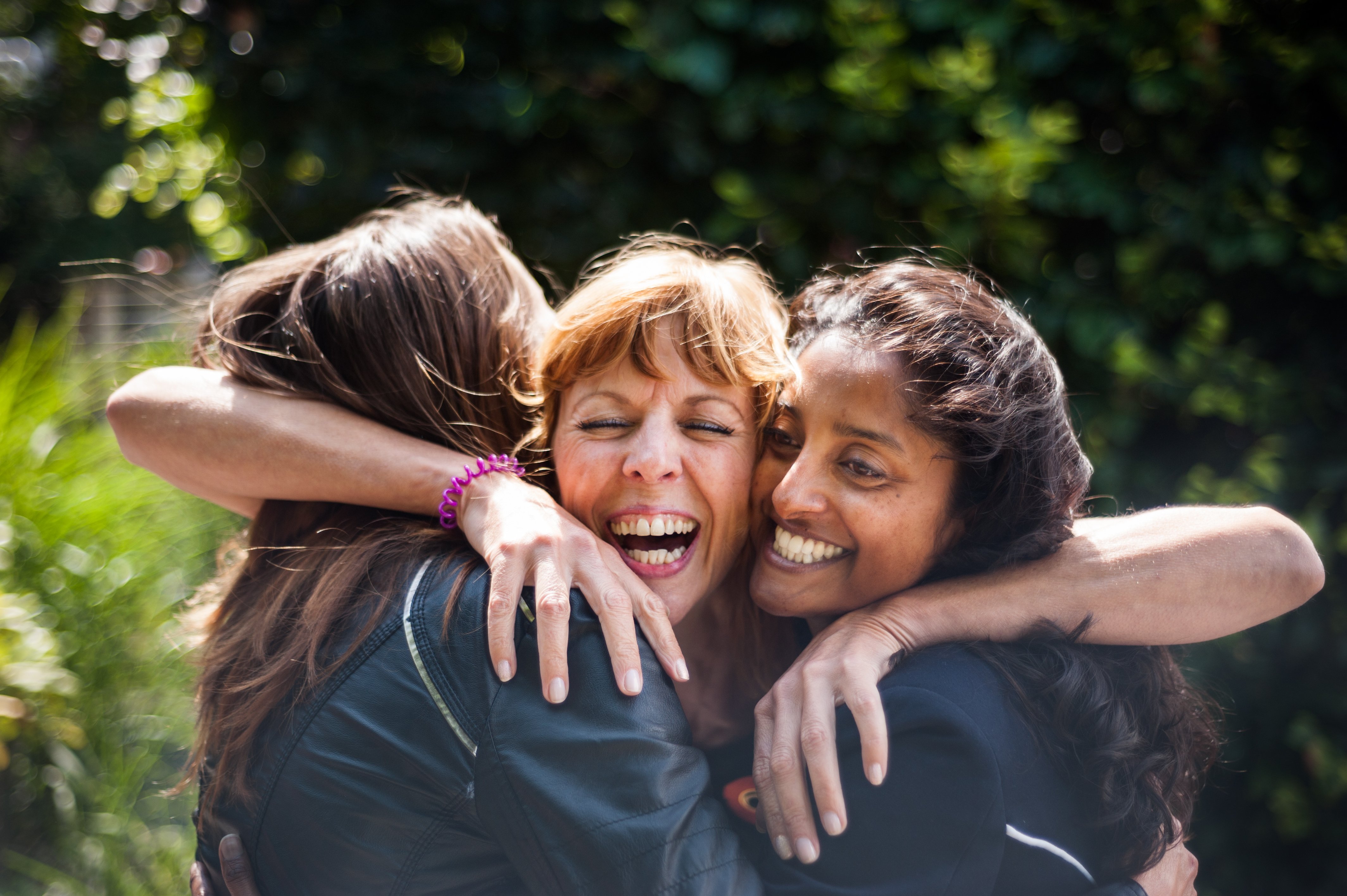 Drei Frauen mittleren Alters umarmen sich und lachen zusammen.